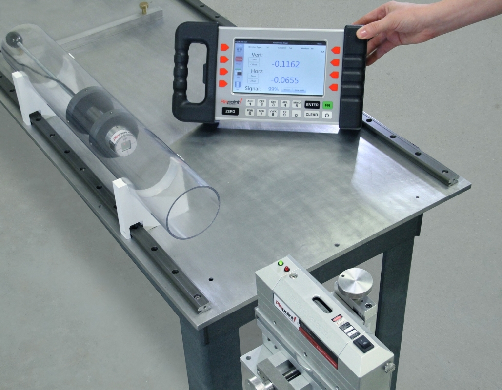 Microgage Bore Receiver Demo Laboratory measurement setup on a metal table: a handheld digital readout displays numerical values beside a clear plastic tube on a support rail.